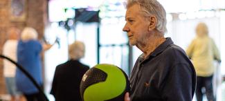 older male sitting in a gym setting, holding a medicine ball